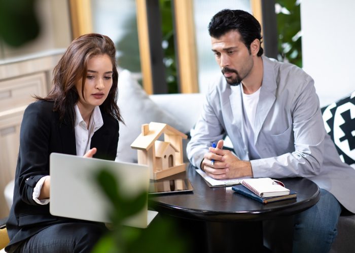 Beautiful woman real estate agent offering and showing online presentation on laptop in office to handsome man.